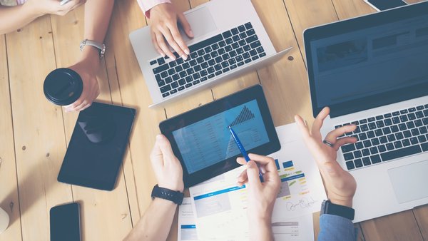 Generisches B&uuml;ro, mehrere H&auml;nde die &uuml;ber einen Tisch greifen Laptops und Tablets auf dem tisch